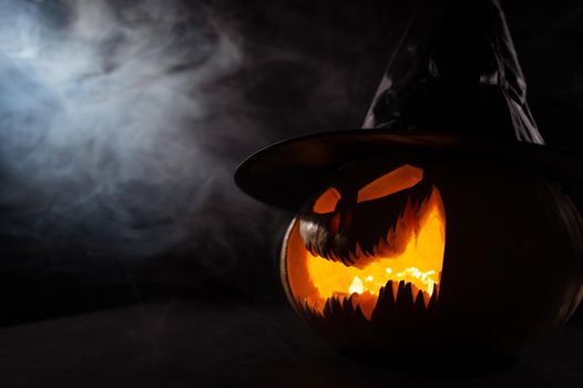 A creepy pumpkin with a carved grimace in the smoke. Jack o lantern in the dark