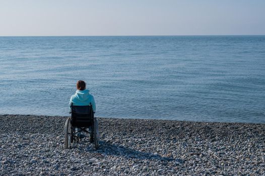 Caucasian woman in a wheelchair on a pebble beach by the sea