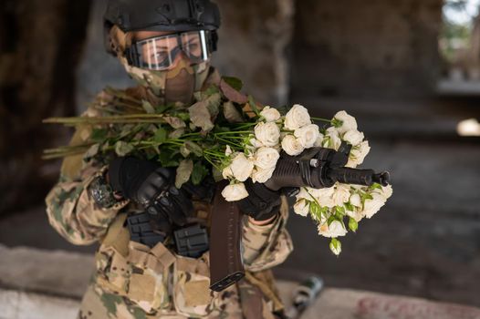 Caucasian woman in military uniform holding a machine gun and a bouquet of white roses