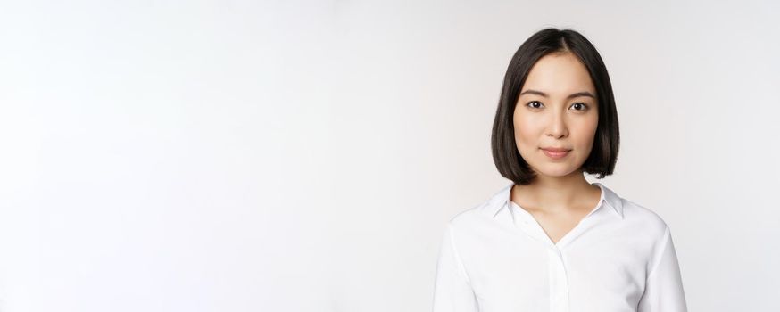 Close up portrait of korean young asian woman, professional, looking confident and assertive at camera, white background. Business people concept