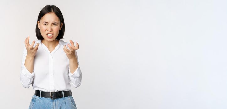 Image of angry pissed off woman shaking from anger, clench hands and grimacing furious, annoyed and outrated, standing over white background.