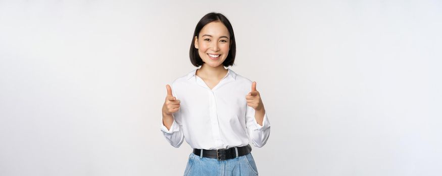 Its you congrats. Smiling attractive asian woman, businesswoman pointing fingers at camera with pleased face, complimenting, inviting you, standing over white background.