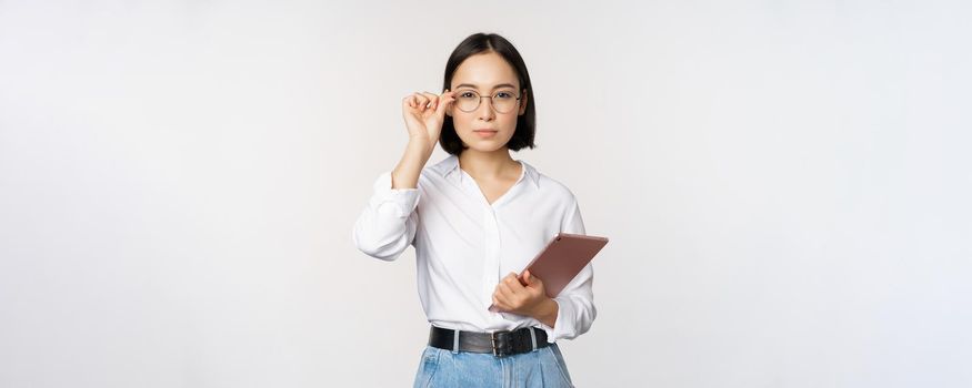 Image of young asian business woman, female entrepreneur in glasses, holding tablet and looking professional in glasses, white background.
