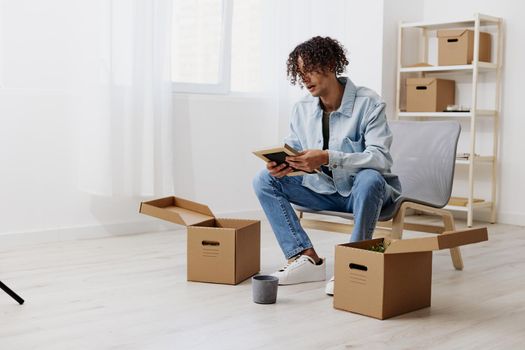 handsome guy sitting on a chair unpacking with box in hand moving interior. High quality photo