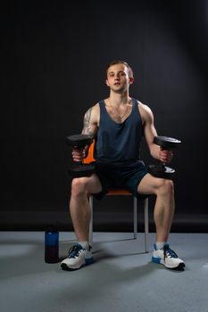 Man on black background keeps dumbbells pumped up in fitness muscle sexy torso, lifting heavy, shirtless weightlifting. Lift handsome adult, people fit sitting on a chair resting after a workout