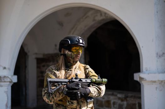Caucasian woman in a protective suit with a machine gun. FA female soldier in a camouflage uniform holds a weapon