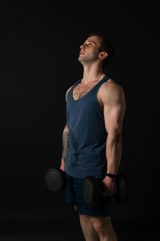 Man on black background keeps dumbbells pumped up in fitness muscle chest body training strong athletic dumbbell, healthy handsome metal, one fit