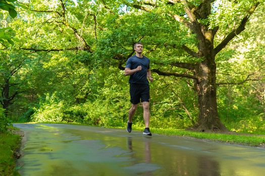 A man athlete runs in the park outdoors, around the forest, oak trees green grass young enduring athletic athlete run sport workout training recreation woods wellbeing. Adult energy running, runners stretches