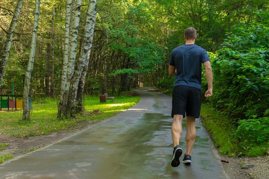 A man athlete runs in the park outdoors, around the forest, oak trees green grass young enduring athletic athlete runner jogger young legs motion, woods running, runners stretches