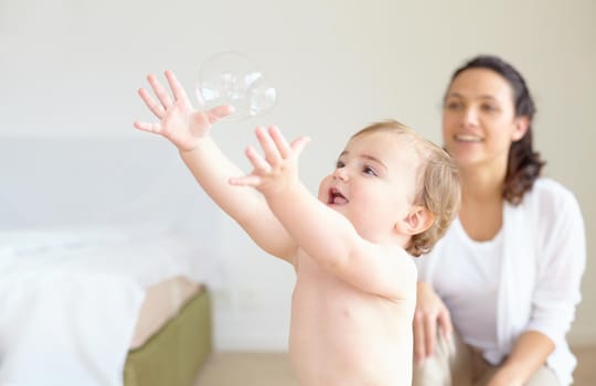 An adorable baby girl reaching for a bubble with her mother smiling in the background - copyspace.