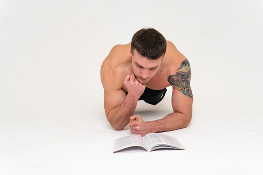 Bodybuilder reads the book on a white background isolated at the bottom of his head on his hands man book muscular, athlete glasses torso background fit. Isolated beach tan