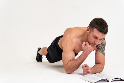Bodybuilder reads the book on a white background isolated at the bottom of his head on his hands man book reading, muscle glasses person body adult, happy sport. Health holding, posing tan