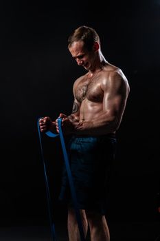 Man on black background keeps dumbbells pumped up in fitness sexy torso, arm man lifting dumbbell, person lifestyle. sportive adult, guy fit With a ribbon in hand, the fitness gum is black