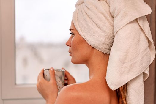 Young serene relaxed woman in spa bath towel drinking hot beverage tea coffee after taking shower bath at home. Beauty treatment, hydration concept