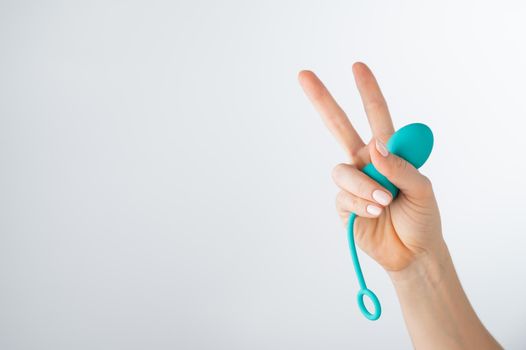 A woman holds a kegel trainer and shows the peace sign. Vaginal eggs on white background.