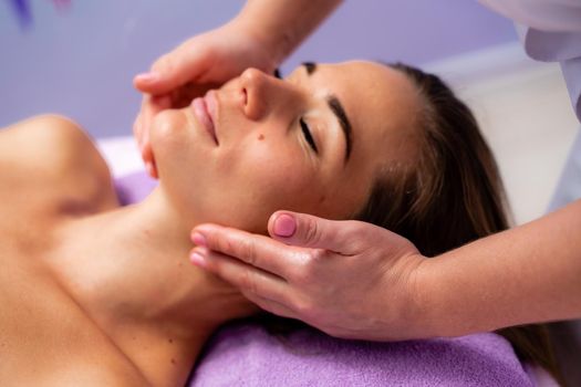 Relaxing massage. European woman getting facial massage in spa salon, side view.