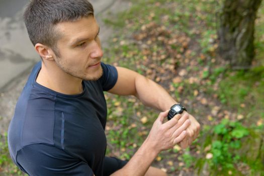 A man looks at the clock time in the park outdoors, around the forest, oaks green grass young enduring athletic athlete. active athlete nature, lifestyle motion, jogging Summer leisure running, feet stretches