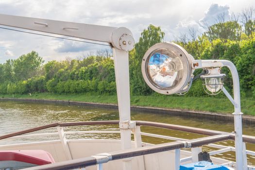 Spotlight on the ship, the ship goes along the river around the trees green during the day in sunny weather blue clouds