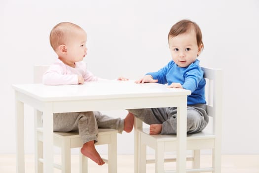 Shot of two adorable little babies sitting together at a table.