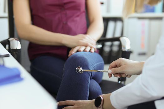 Close-up of doctor neurologist checking knee reflexes of female patient with percussion hammer in clinic. Neurology, checkup, medicine, diagnostics concept