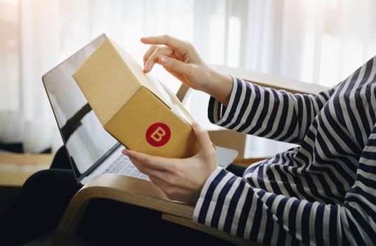 Online merchandising business idea, beautiful girl holding a parcel delivery box and using a computer to input Track And Trace parcel numbers to customers