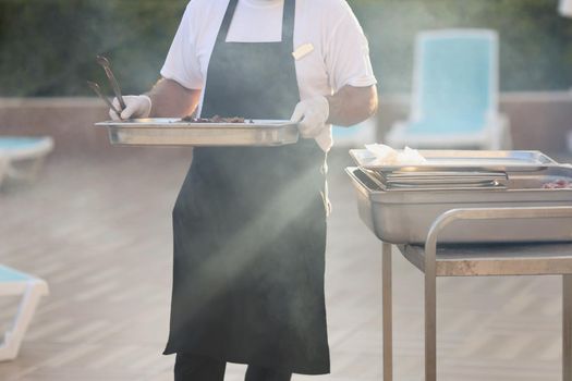 Close-up of chef carry cooked meal, metal construction for frying food, do grill, picnic outdoors, frying meat and vegetable. Street food, barbeque concept