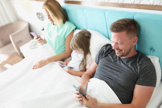 Close-up of family stare in smartphone, morning in bed with devices, kill time. People addicted to modern technologies, bored. Social media, addict concept