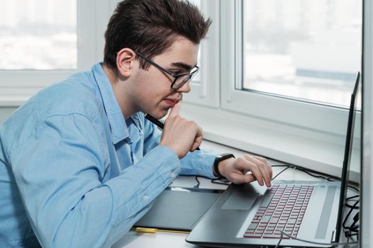 young male designer in glasses working on a professional graphics tablet with a pen