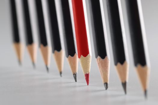 Close-up of tips of pencils put on paper in strict order, unique red among ordinary black, idea of creativity and uniqueness. Stay different, lead concept