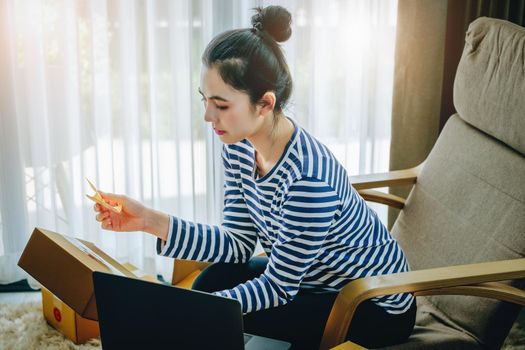 Online merchandising business idea, beautiful girl holding a parcel delivery box and using a computer to input Track And Trace parcel numbers to customers