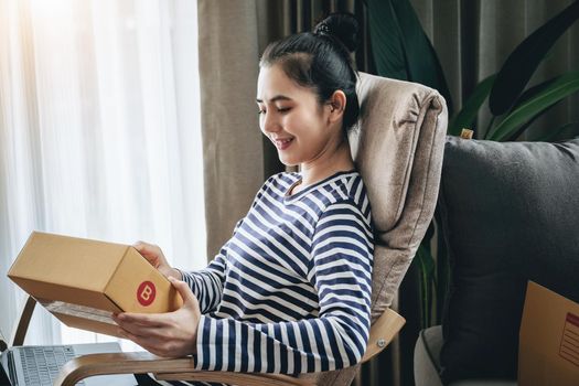 Online merchandising business idea, beautiful girl holding a parcel delivery box and using a computer to input Track And Trace parcel numbers to customers