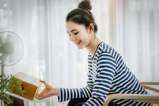 Online merchandising business idea, beautiful girl holding a parcel delivery box and using a computer to input Track And Trace parcel numbers to customers