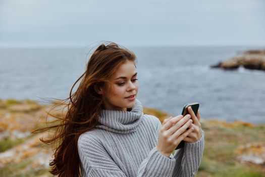 woman in a gray sweater with a phone in her hands by the ocean. High quality photo