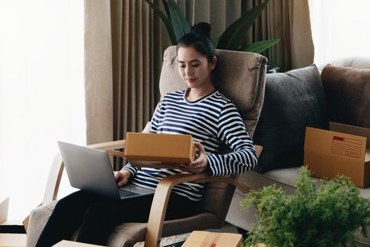 Online merchandising business idea, beautiful girl holding a parcel delivery box and using a computer to input Track And Trace parcel numbers to customers