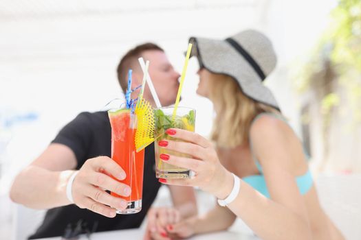 Portrait of woman and man kissing and having cooling cocktails, couple resting on luxury resort, chill, swimming pool. Vacation, toast, holiday concept