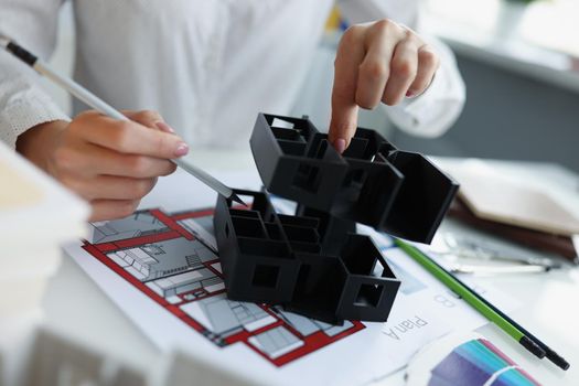 Close-up of female architect work on house project, use miniature house toy for plan improvement. Blueprint on table, talented designer. Creative concept