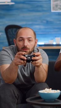 Modern interracial couple playing video game on TV with console and joysticks at home. Multi ethnic people having fun with controller and technology in living room, looking at camera