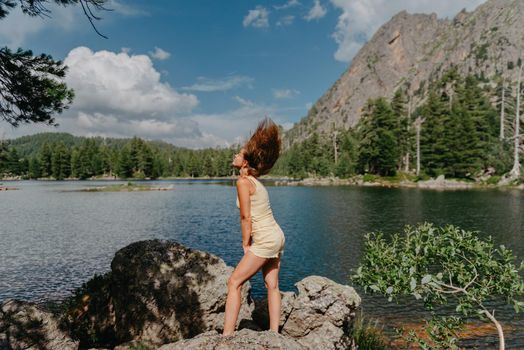 Tourist girl enjoys the magical view of the lake, coniferous forest and magical view sitting on big stone on the shore of a turquoise lake in the mountains. Hiking in the Natural Park. Black lake.