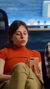 Modern interracial couple using technology on couch at home. Caucasian woman holding smartphone while african american man working on laptop sitting together in living room on sofa