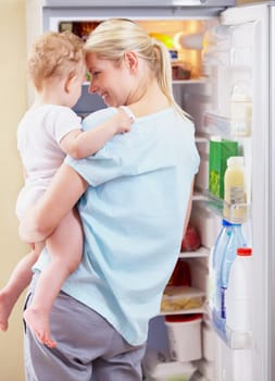 A mother standing in front of the fridge and holding her baby in her arms.