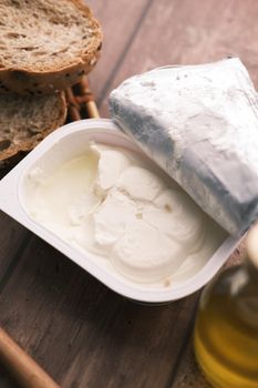 cheese cream in a container with bread and oil on table .