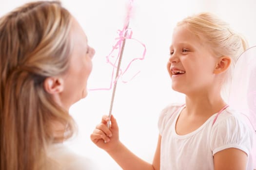 A smiling girl dressed up as a fairy and holding a wand standing infront of her mother.