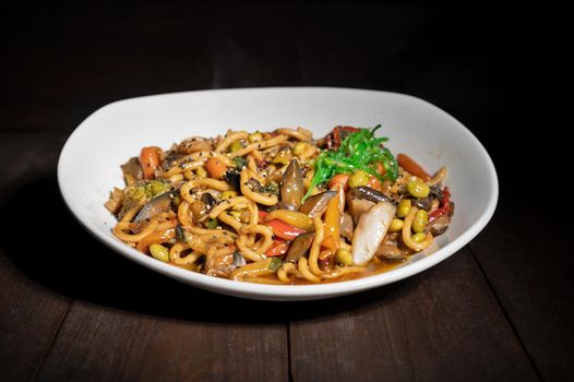 Asian vegetarian food udon noodles with shiitake mushrooms, sesame and pepper close-up on a plate on the wooden table. High quality photo
