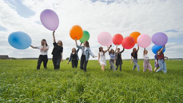 Girls friends are walking across the field with large balloons and colorful balloons