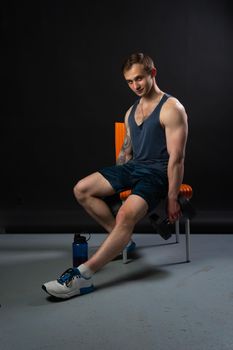 Man on black background keeps dumbbells pumped up in fitness sexy arm weight exercise athletic heavy, lifestyle. Young skin metal, one fit sitting on a chair resting after a workout