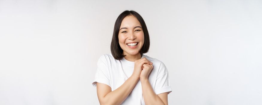 Portrait of beautiful korean woman with healthy white smile, laughing and looking happy at camera, standing in tshirt over white studio background.