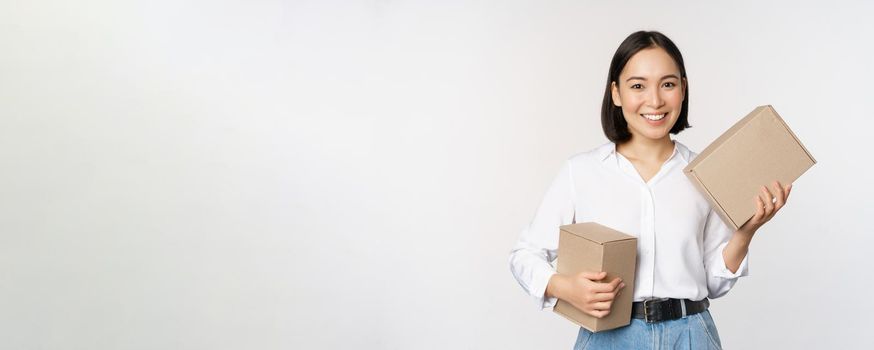 Concept of shopping and delivery. Young happy asian woman posing with boxes and smiling, standing over white background.