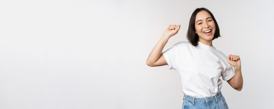 Happy dancing korean girl posing against white background, wearing tshirt.