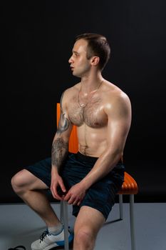 Man on black background keeps dumbbells sits on an orange chair resting pumped pumped up in fitness bodybuilding arm muscular person lifestyle. sportive metal, people fit