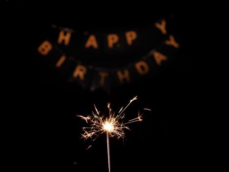 Close-up of sparkler on black isolated background with inscription Happy Birthday in golden letters. Footage is shot in 4k from a tripod under artificial professional lighting